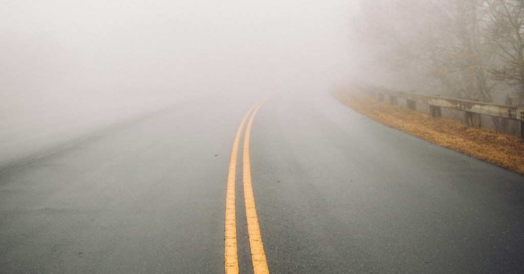Yellow double line in the center of a road, with dense fog ahead. A symbol of starting off a relationship, noticing issues, but continuing on anyway.