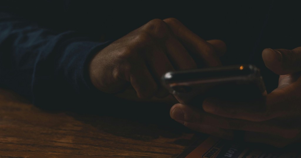 Man in a dark room texting in secrecy, so his wife can not see what he is doing.